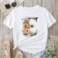 White t-shirt with floral design on a wooden surface with sandals and jeans.