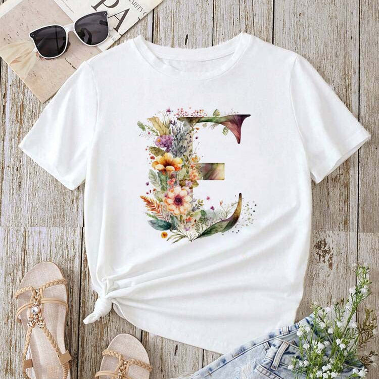 White t-shirt with floral design on a wooden surface with sandals and jeans.
