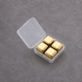 Four square gold-colored magnetic bottle stoppers arranged inside an open translucent plastic storage case on a textured gray surface.