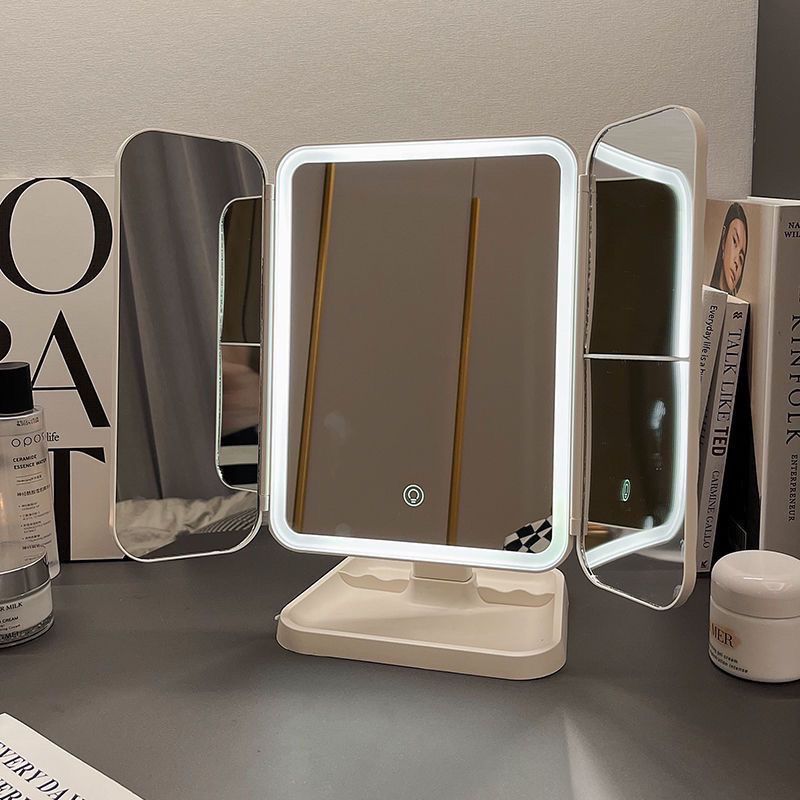 Lighted makeup mirror with three folding sides on a surface with books on the backround