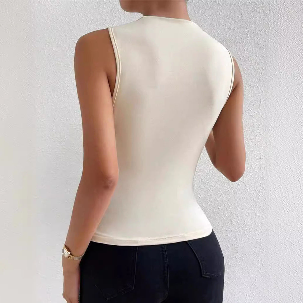 Person wearing an apricot sleeveless top and black pants against a white wall